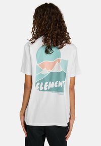 Witte T-shirt met een kleurrijke afbeelding van bergen en een zon op de achterkant. Het ontwerp bevat teal, roze en witte accenten.