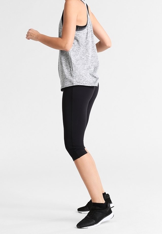 Top in tessuto grigio sportivo e leggings neri a tre quarti, caratterizzati da un tessuto morbido, un design aderente e scarpe da ginnastica nere con dettagli testurizzati.
