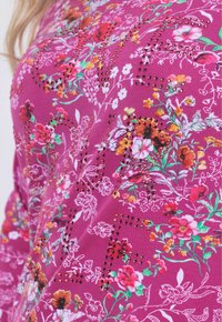 Lila Kleidungsstück mit floralem Muster, das mit bunten Blumen verziert ist und durch metallische Akzente überall für zusätzliche Details geschmückt wird.