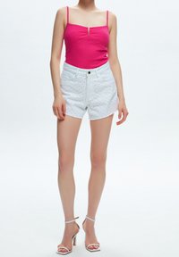 Top a fascia rosa con spalline sottili e un piccolo dettaglio a bottoni, abbinato a pantaloncini bianchi con fori a occhio e orlo sfilacciato.