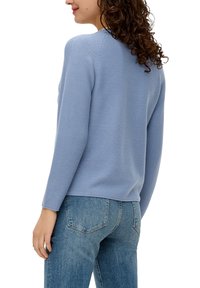 Lichtblauwe trui met een getextureerd breiontwerp, ronde hals en lange mouwen, gecombineerd met blauwe jeans. Zichtbare naaddetails bij de schouders.