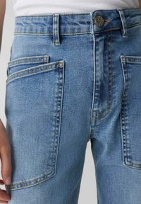 Jeans in denim azzurro chiaro con vita alta, caratterizzati da tasche frontali e posteriori doppie, cuciture visibili e chiusura con bottone in metallo.