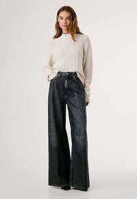 Vit kabelstickad tröja med ribbade muddar och röda detaljer, kombinerad med högmidjade vida svarta denimjeans med framfickor.