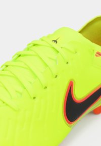 Nike fodboldstøvle i lys neongul, med sort swoosh-logo og accenter, struktureret overflade og flade snørebånd.