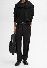 Czarny wełniany sweter z kołnierzem, w połączeniu z czarnymi spodniami o wysokim stanie. Wykończony czarnym paskiem i czarnymi skórzanymi butami.