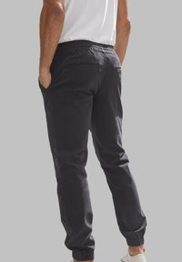 Donkergrijs joggerbroeken met elastische boorden, een trekkoord in de taille en zakken. Gemaakt van zacht materiaal met een gladde textuur.