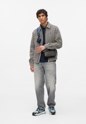 Tekstūrēta, gaiši pelēka jaka ar apkakli, kombinēta ar tumši zilu kreklu un brīviem pelēkiem džinsiem. Melna soma ar logo akcentiem un zilu siksniņu.