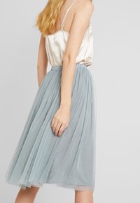 Gonna midi in tulle azzurro chiaro con design plissettato e vita elasticizzata, abbinata a un top in satin senza maniche di colore avorio.