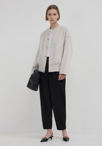 Veste surdimensionnée gris clair avec des boutons-pression, ourlet côtelé et poches avant, associée à un pantalon noir et un petit sac à main noir.