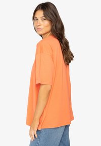 Loose-fitting t-shirt in bright orange cotton, featuring dropped shoulders and a straight hem, paired with light blue jeans.
