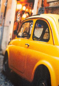 Vintage gele auto met ronde hoeken, opvallende grille aan de voorkant en klassieke ramen, geparkeerd op een straat van kasseien. Opvallende texturen zichtbaar.