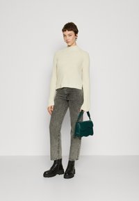 Maglione lavorato a maglia avorio, jeans grigi a gamba dritta, stivali neri con lacci e una borsa texturizzata turchese con un bordo superiore ondulato.
