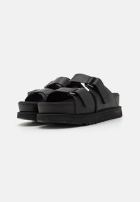Sandales noires avec une semelle en caoutchouc épaisse, dotées de deux sangles ajustables et d'un amorti profilé pour le confort. Finition mate, design minimaliste.