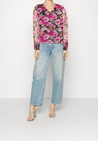 Blusa floreale con scollo a V, decorata con fiori rosa e bianchi su uno sfondo nero; abbinata a jeans a gamba larga azzurri e tacchi a righe.