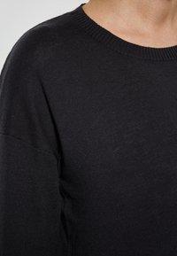 Schwarzer Pullover mit Rundhalsausschnitt, geripptem Kragen und weichem Strickstoff. Verfügt über eine lockere Passform und ein minimalistisches Design ohne Muster.