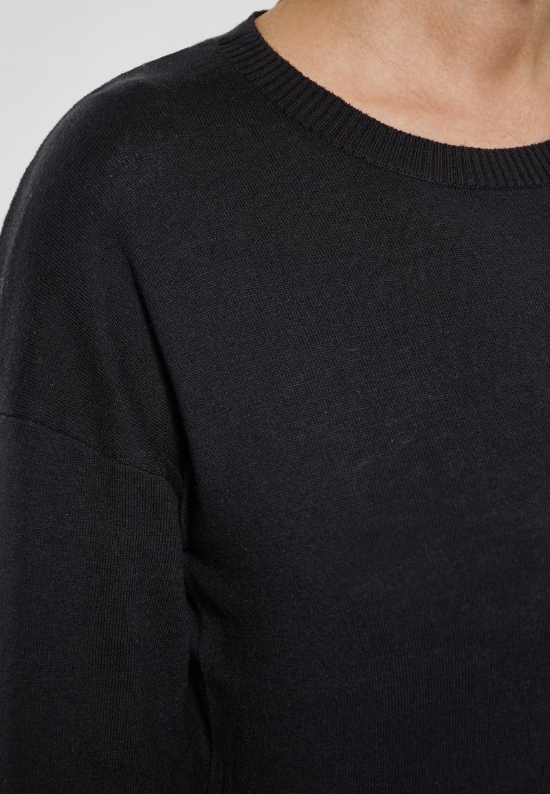 Svart tröja med rund hals, ribbat krage och mjukt stickat material. Har en avslappnad passform och en minimalistisk design utan mönster.