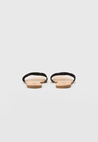 Zwarte platte sandalen met dunne banden en een natuurlijk gekleurde zool. Minimalistisch ontwerp met open tenen en achterkant, die gladde texturen toont.