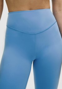 High-waisted leggings van lichtblauwe stof, gladde textuur en een aansluitend ontwerp met platte naden en subtiele stikseldetails.