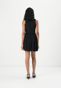 Robe noire sans manches avec un corsage ajusté et une jupe évasée. Détails de taille smockée, tissu lisse, portée avec des sandales à talons noires.