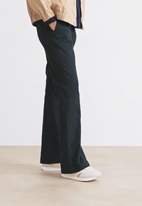 Fekete, egyenes szabású nadrág, sima anyagból készült, oldalsó zsebekkel, világos színű slip-on cipőkkel párosítva.