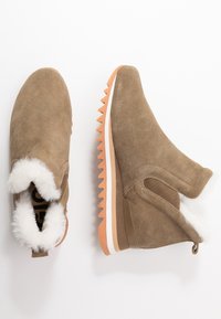 Bottines en daim marron avec doublure en fausse fourrure blanche, panneaux latéraux élastiques et semelle en caoutchouc orange texturé. Présente un design moderne à enfiler.