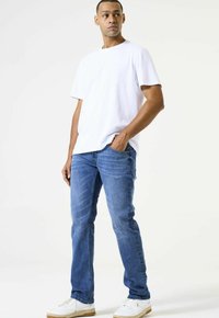 Camiseta de algodón blanca, jeans de mezclilla azules y zapatillas blancas con suelas beige, vistas de frente, destacando la vestimenta casual y el ajuste.