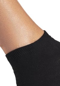 Schwarze gerippte Knöchelsocke mit einer strukturierten Oberfläche, ausgestattet mit einem weichen, elastischen Bündchen, das den Knöchel eng umschließt. Glatte Haut ist darüber sichtbar.
