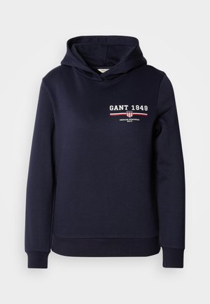 Mörkblå huvtröja i mjukt tyg med vit text "GANT 1949" och ett randigt grafiskt detalj i rött och vitt.