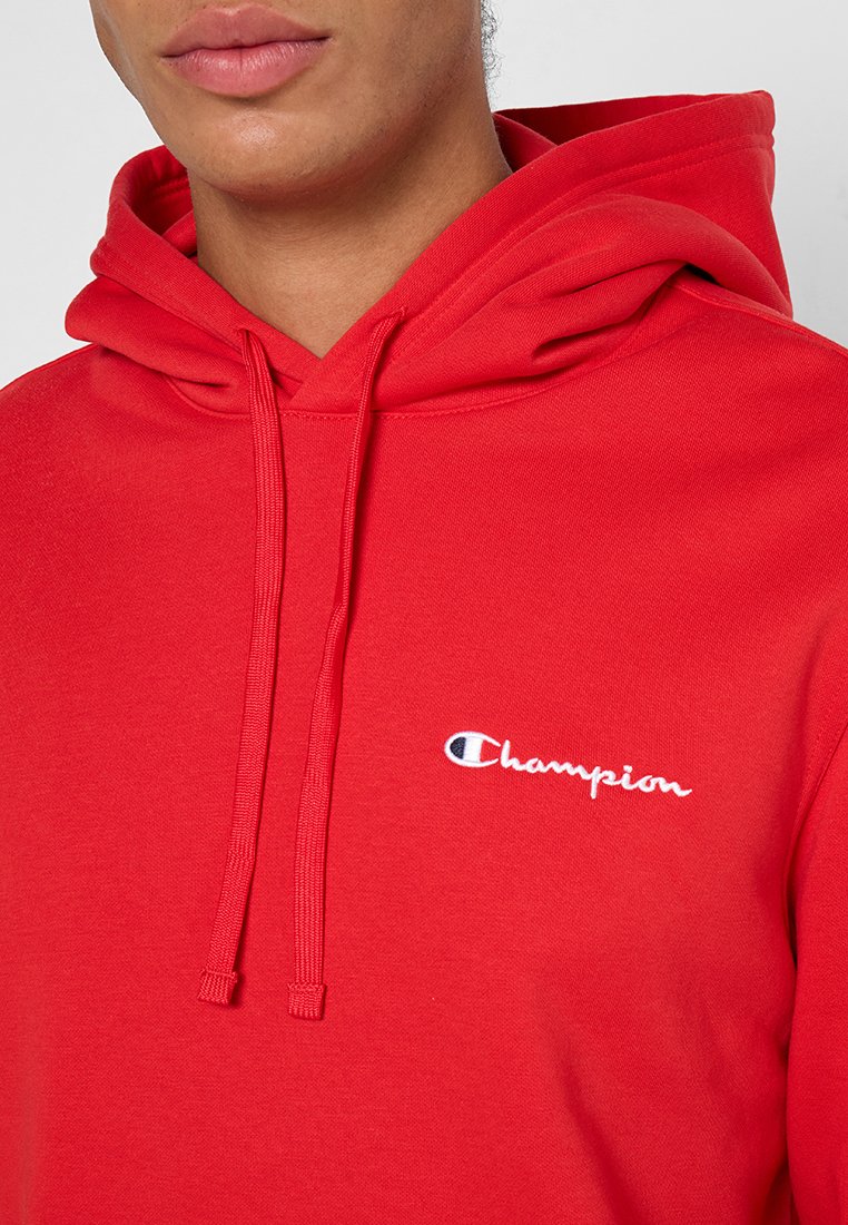 Persona que lleva puesta una sudadera roja de Champion con cordones y el logotipo de la marca bordado en el pecho.