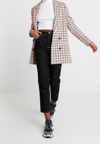 Rutig blazer i rosa och svart med dubbelknäppta knappar, kombinerad med svarta raka jeans och blå sportskor.