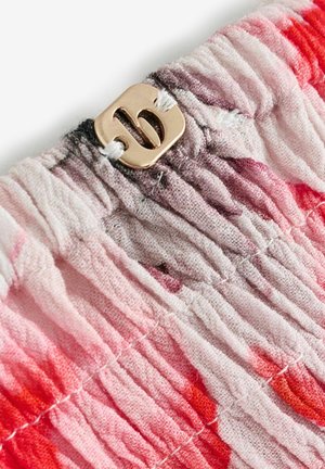 Elastická tkanina v odstínech růžové a červené, s čtvercovou zlatou kovovou přezkou se stylizovaným logem „B“ uprostřed. Texturovaný a nabraný design.