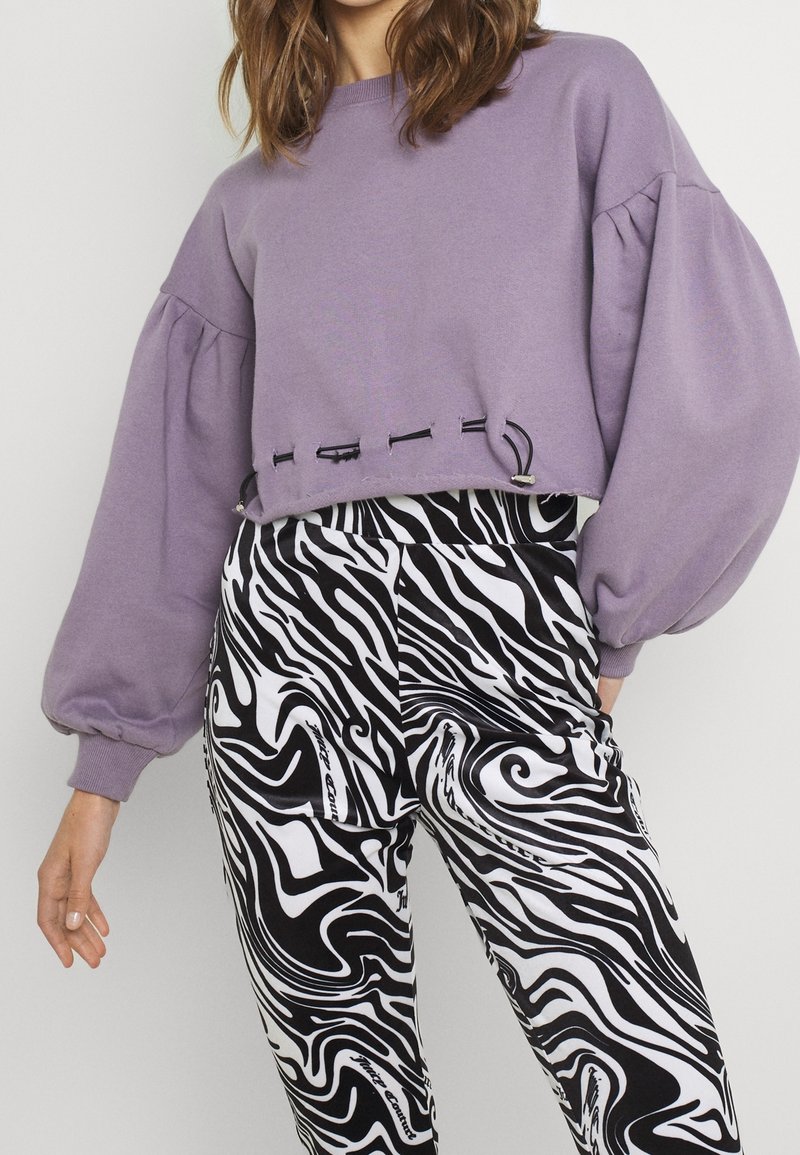 Personne portant un sweat court lilas avec des manches ballon et un pantalon à motif abstrait noir et blanc.