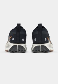 Schwarze Sportschuhe mit strukturierter Oberseite, Mesh-Akzenten, kontrastierenden orangen Details und robuster weiß-schwarzer Außensohle. Zuglasche an der Ferse.