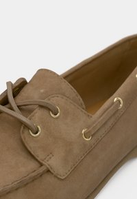 Καφέ παπούτσι από σουέτ με στρογγυλεμένο σχήμα, διαθέτει χρυσαφί μεταλλικά ριγέ, δέσιμο με κορδόνια και εμφανείς λεπτομέρειες με ραφές. Ομαλή υφή.