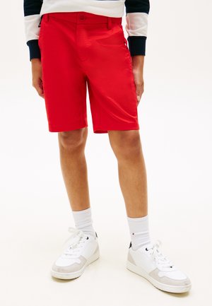 Person wearing bright red knee-length shorts, white socks, and white sneakers, standing on a plain white background.