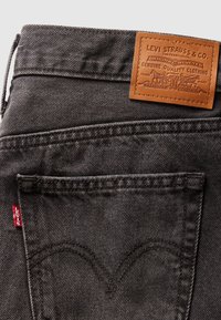 Poche de jean en denim noir avec un onglet rouge Levi's et un patch de marque en cuir marron Levi Strauss & Co. au-dessus.
