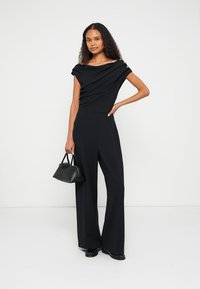 Black jumpsuit with draped off-shoulder design, fitted bodice, and wide-leg pants. Features subtle gold accent buttons. Classic fabric texture.