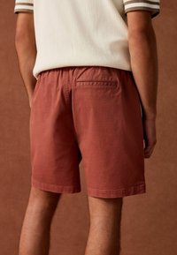Roodbruine shorts met een elastische tailleband en een achterzak. Gemaakt van een zachte stof, hebben ze een gladde textuur en een eenvoudig ontwerp.