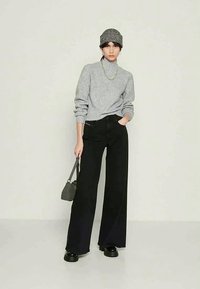 Camisola cinzenta de malha, jeans pretos de perna larga, botas pretas com plataforma. Os acessórios incluem um boné cinzento com padrão e uma pequena mala cinzenta.