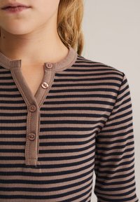 Braun und navy gestreifte Langarmbluse mit rundem Halsausschnitt und Dreiknopfleiste, aus weichem Rippmaterial.