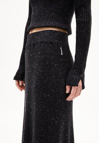Schwarzes, geripptes Strick-Zweiteiler-Set, bestehend aus einem cropped Pullover mit langen Ärmeln und einem hochtaillierten Rock, akzentuiert mit gesprenkelten Details.