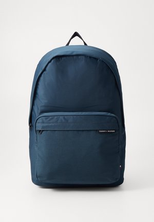 Marineblauwe Tommy Hilfiger rugzak met een voorvak met rits en een zwart bovenhandvat op een witte achtergrond.