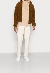 Brown corduroy jacket, beige hoodie, white pants, and white sneakers. The jacket has a zip and elastic cuffs; hoodie features drawstrings.