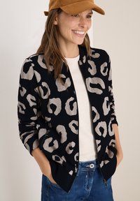 Veste bomber à imprimé léopard en noir et crème, dotée d'une fermeture éclair à l'avant, de poches latérales, de poignets et d'un ourlet côtelés, associée à un haut léger et à un jean.