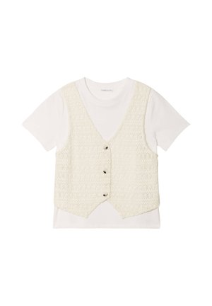 Häkelwesten in Creme mit fünf Knöpfen über einem weißen T-Shirt mit kurzen Ärmeln. Die Weste hat ein strukturiertes Muster und einen abgerundeten Saum.