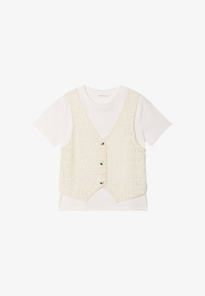 Gehaakt crèmetint vest met vijf knopen over een wit T-shirt met korte mouwen. Het vest heeft een gestructureerd patroon en een gebogen zoom.