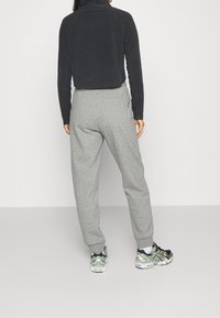 Schwarze, gekürzte Fleecejacke mit hohem Kragen, kombiniert mit grauen Jogginghosen. Die Schuhe haben ein schwarzes und grünes Design mit weißen Sohlen.