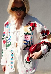 Tikkitud valge kardigan, millel on punased, sinised ja rohelised lillemustrid. Sidumine kaela juures, ees kaks taskut ja pehme tekstuur.