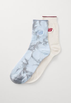 Dva para čarapa: jedan je svijetloplave boje s tie-dye uzorkom i plavim logotipom, dok su drugi krem boje s teksturiranim dizajnom i crvenim logotipom.
