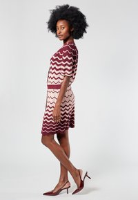 Neulemekko, jossa on aaltoilukuviota viininpunaisissa ja vaalean kermanvärisissä sävyissä, lyhyet hihat, istuva vyötärö ja aaltoileva helma. Yhdistetty viininpunaisiin korkokenkiin.